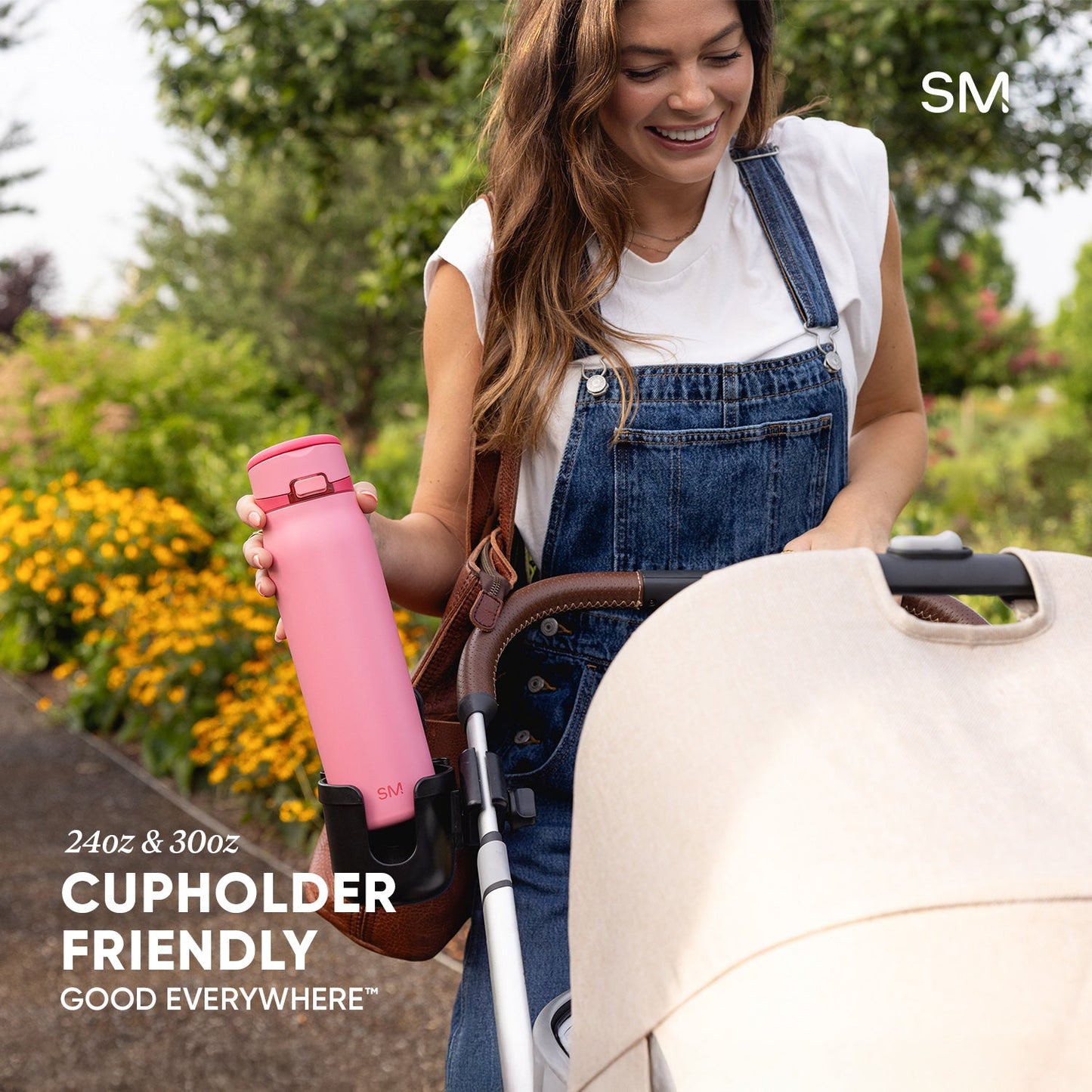 Woman in denim dress holding bright pink Simple Modern water bottle next to stroller in blooming garden. Text reads "24oz & 30oz Cupholder Friendly Good Everywhere."