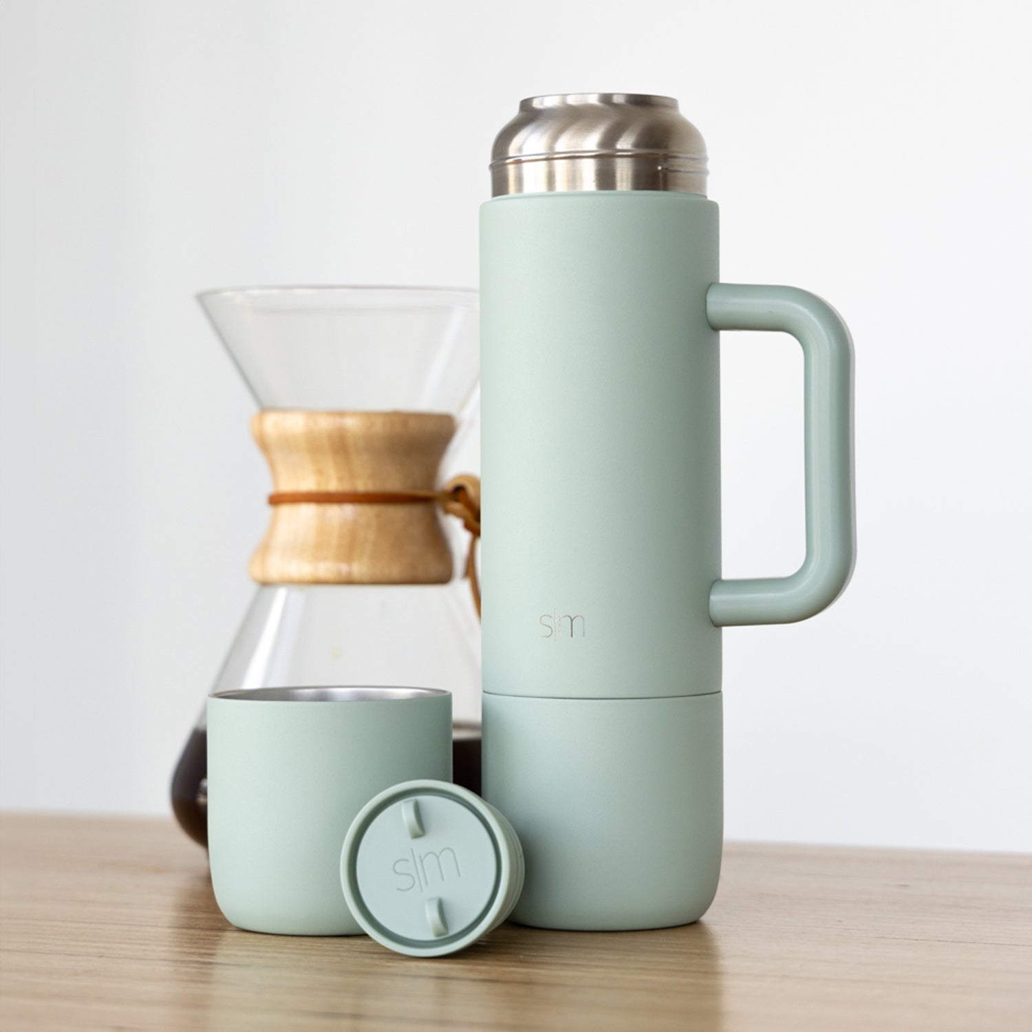 Sage green insulated tumbler with handle, matching cup, and circular lid on a neutral background